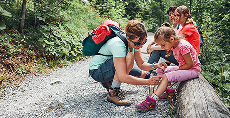 Woman with three children in the outdoors putting a bandaid on the knee of a child 